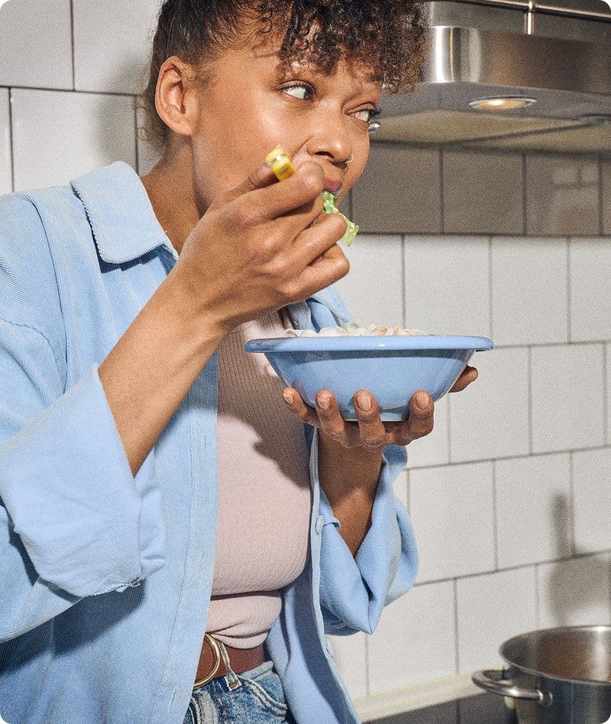 En kvinde spiser morgenmad fra en skål i et lyst køkken.